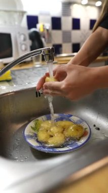 Bir insan özenle taze patatesleri akarsu altında bir mutfak lavabosunda iyice yıkar.