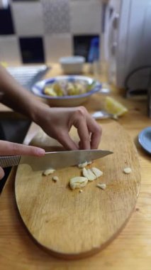 Tecrübeli bir şef, sıcak mutfak ortamında ahşap bir kesme tahtasının üzerinde ustalıkla taze sarımsak doğruyor.