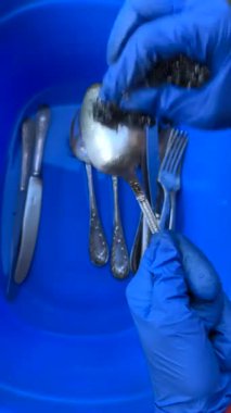 Koruyucu eldiven giyen eller, mavi bir leğenin içindeki gümüş takımları onarmak için titizlikle kullanırlar.