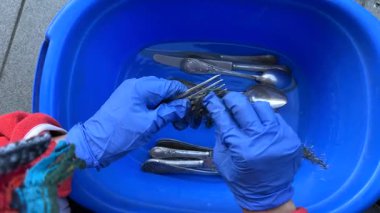Bir kişi gümüş takımları mavi bir leğende temizler, günlük rutinlerde sürdürülebilirliği ve temizliği teşvik eder.