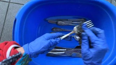 Çalışkan bir insan mavi bir leğende gümüş takımları temizler, günlük kullanım için hijyenin önemini vurgular.