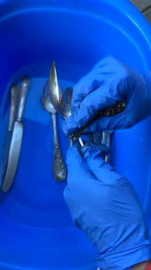 Mavi bir leğende gümüş takımları titizlikle temizleyen, kendini işine adamış ve titiz bir el kamerası görüntüsü.