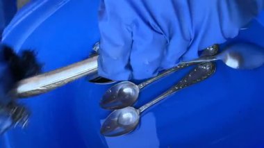 Eller, temizlik ve temizliğin önemini vurgulayan çeşitli mutfak aletlerini mavi bir kabın içinde temizler.