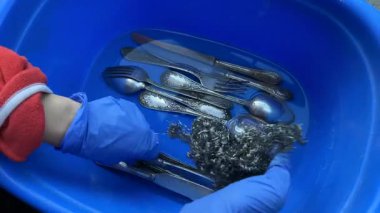 Bir insan mavi bir havuzda deniz yosunu kullanarak gümüş takımları temizler ve titiz temizlik teknikleri gösterir..