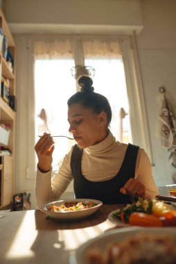 Güneşli, neşeli bir odada nefis ve lezzetli bir yemeğin tadını çıkaran sağlıklı beslenmenin altını çizen bir kadın.