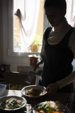 Lezzetli bir yemek tabağı hazırlayan bir kadın yemek sanatını taze malzemelerle dolu sıcak bir mutfakta sergiliyor.