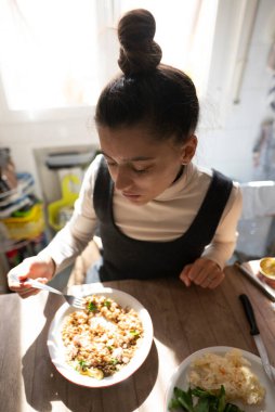 Bir kadın sıcak bir mutfak masasında lezzetli ve besleyici bir yemek kasesinin tadını çıkarıyor.