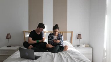 Bir çift, rahat yataklarında, modern yatak odasındaki aletleriyle meşgul olarak, kaliteli vakit geçirmekten mutlu olurlar.