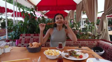 Bir kadın, hayat dolu, canlı bir restoranda kızartma ve çayla ızgara yemekten zevk alır.