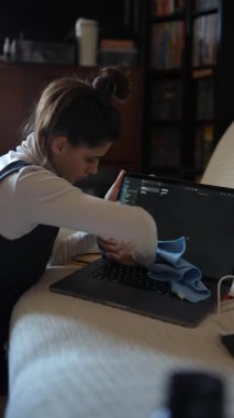 Sıcak bir ev ortamında, bir kadın mikrofiber bez kullanarak özenle dizüstü bilgisayarını temizlerken odaklanır.