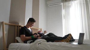 Genç bir adam rahatça yatağında aletler ve rahat bir atmosferle vakit geçirir.