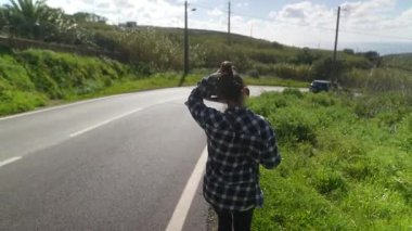 Genç bir kadın dolambaçlı bir yolda rahatça yürüyor. Çevresi güzel, gür yeşilliklerle çevrili.