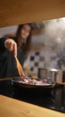 Sıcak bir mutfakta, genç bir insan sobada soğan pişirir, lezzeti arttırmak için baharat ekler.