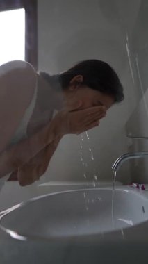 Huzurlu bir anda, bir kadın nazikçe yüzünü güzel, parlak ve davetkar bir banyo alanında temizler.