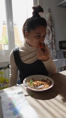 Genç bir kadın evde besleyici bir yemek yiyor. Doğal ışık büyüleyici yemek alanını aydınlatıyor.