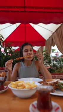 Bir kadın rengarenk ve canlı bir açık hava restoranında leziz ızgara şiş yiyor.
