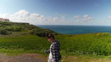 Etrafı yemyeşil yeşilliklerle çevrili, okyanus kıyısında sakin bir yürüyüşün tadını çıkarıyorum. Uzakta görünen bir deniz feneri.