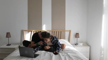 Sıcak bir yatak odasında, genç bir çift laptoplarını birlikte kullanırken sevgi dolu bir şekilde iletişim kuruyor.
