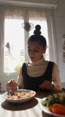 Neşeli bir kadın canlı ve besleyici bir yemekten zevk alıyor. Parlak, güneşli bir mutfak ortamında rahat bir yerde.