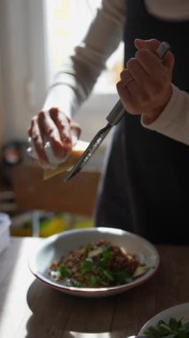 Bir şef sıcak, neşeli bir mutfakta taze sebze ve tahıl tabağının üzerinde peynir rendeliyor.