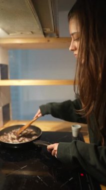 Şık ve modern bir mutfakta hevesle yemek pişiren genç bir insan kızartma tavasında malzemeleri ustalıkla karıştırıyor.