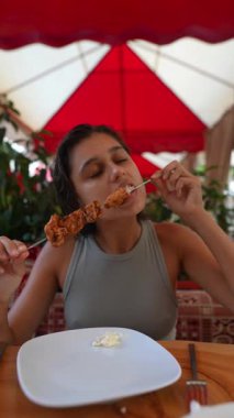 Çevresi yemyeşil ve arkadaşlarıyla çevrili canlı bir açık hava restoranında şişin tadını çıkaran biri.