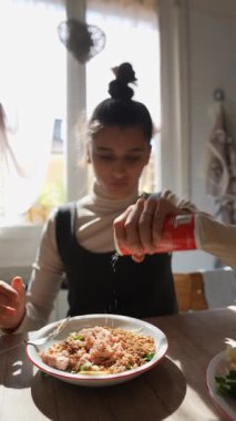 Sıcak bir mutfakta, genç bir kadın tabağını besleyici bir yemek için taze, renkli malzemelerle doldurur.