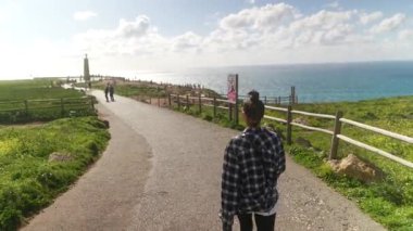 Bir insan sakin bir şekilde güzel, manzaralı bir sahil yolunda yürüyor, etrafındaki çarpıcı okyanus manzarasının tadını çıkarıyor.