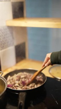 Bir insan yemek pişirirken tavada taze kesilmiş sebzeleri hararetle karıştırıyor.