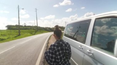 İşaretli gömlek giyen bir kadın, güzel manzaralı bir sahil yolu boyunca açık havanın tadını çıkarıyor.