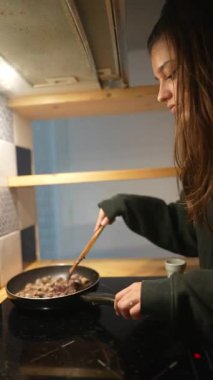 Genç bir kadın, şık bir mutfakta yemek pişirme sürecinin tadını çıkarırken kızartma tavasında ustalıkla yemek pişiriyor.