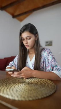 Genç bir kadın cep telefonuyla samimi ve davetkar bir ortamda özenli ve düşünceli bir şekilde iletişim kuruyor.