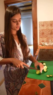 Bir kadın rahat mutfağında taze, gevrek salatalıkları ustalıkla doğruyor ve etkileyici mutfak yeteneklerini sergiliyor.