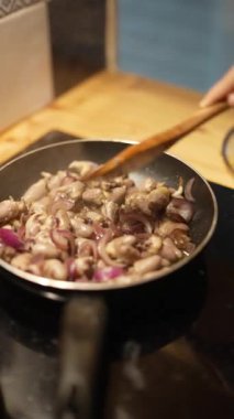 Bir şef tavada soğan ve sarımsak karıştırıyor, aşçılık teknikleri ve taze malzemeler sergiliyor.