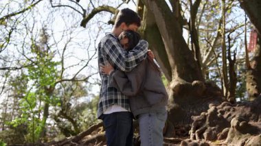 Bir çift, açık havada sakin bir ortamda kucaklaşırken samimi ve sevgi dolu bir anı paylaşmaktan zevk alır.