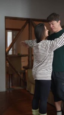 Sevgi dolu bir çift kucaklaşmayı ve parlak gülümsemeleri paylaşıyor sıcak ve davetkar bir ev ortamında, neşeyle dolu.