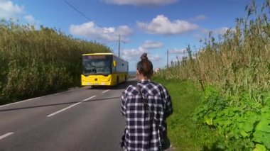 Bir insan, yemyeşil ve parlak mavi gökyüzüyle çevrili güzel bir yolda rahatça yürür.