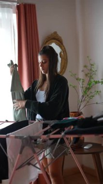 Güneşli bir sabahta, genç bir kadın çamaşırlarını pencerenin kenarından yıkıyor ve güzel ışığın içeri girmesine izin veriyor.