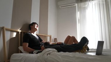 Sıcak, güneşli bir odada, bir çift, rahat yataklarında, dijital cihazlarıyla meşgul olarak, kaliteli boş vakitlerini paylaşıyor.