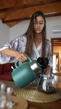 Bir insan ustalıkla ve dikkatle demlenmiş taze kahveyi ahşap bir masaya yerleştirilmiş cam bir kavanoza doldurur.