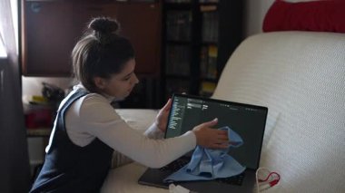 Çalışkan genç bir kadın, ev ortamında bir bezle dizüstü bilgisayarını temizliyor.