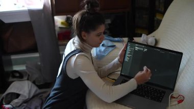 Odaklanmış genç bir kadın, gündelik, rahat bir ortamda dizüstü bilgisayarı üzerinde çalışıyor.