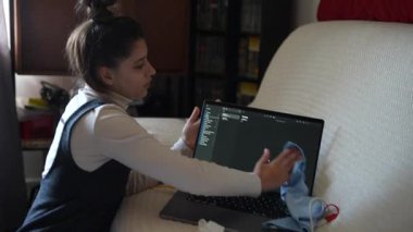 Genç bir kadın evde çalışırken bilgisayarını temizliyor, rahat ve rahat bir çalışma ortamı yaratıyor.