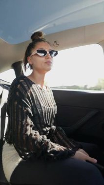 Bir arabanın arka koltuğunda şık giyinmiş bir kadın eşsiz ve büyüleyici havasını sergiliyor.