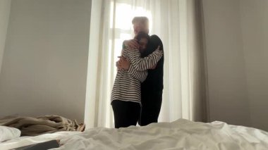 Bir çift, yumuşak ışıklandırılmış ve rahat bir yatak odası ortamında çok hassas ve tatlı bir anı paylaşıyor.