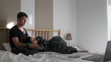 Sıcak, samimi bir sahne, iki kişinin yatakta mutlu bir an paylaştığı, yakınlarda bir dizüstü bilgisayarla