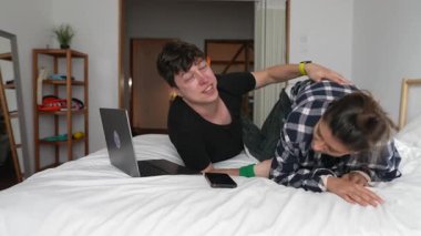Oyuncu bir çift laptoplarıyla rahat bir yatakta yakınlık ve neşe göstererek birlikte eğleniyor.