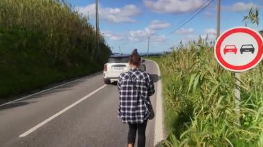 Bir insan, yemyeşil yemyeşil ve açık mavi gökyüzü ile çevrili, dolambaçlı, manzaralı bir yolda rahatça dolaşır.