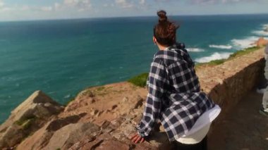 Dalgın bir insan uçurumlarda durur, sakin okyanusa bakar, doğayı ve güzelliği kucaklar.