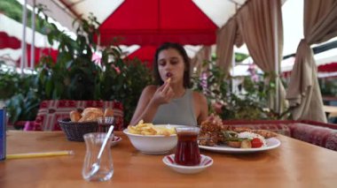 Genç bir kadın, canlı dekorlarla süslenmiş sıcak bir açık hava restoranında lezzetli ve tatmin edici bir yemeğin tadını çıkartıyor.